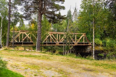 İsveç Laponya 'nın geniş ormanlık arazisinde bulunan küçük bir nehri geçen eski metal köprü, yeşil ve sarı yaprakların arasında yaşlanan altyapıyı gösteriyor.