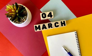 Tahta küplere 4 Mart. Yanında beyaz bir defter, bir kalem ve bir saksı çiçeği var. Mart ayı takvimi..