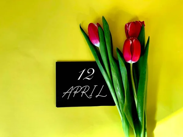 April Black Paper Next Red Tulips Yellow Background Corner Photo — Stock Photo, Image