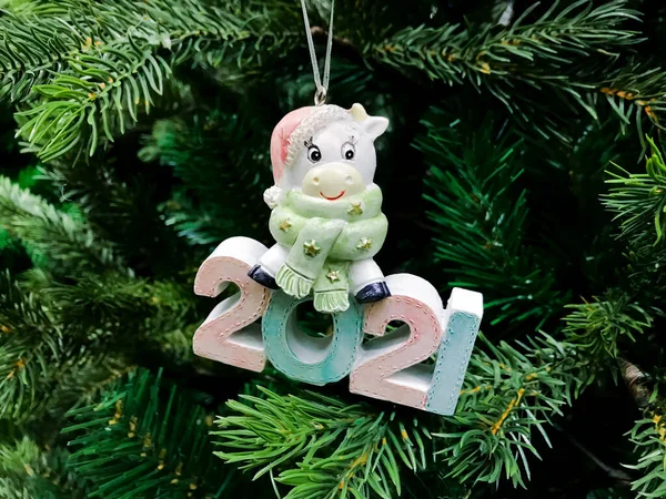 Şapkası ve atkısı olan mutlu beyaz ineğin sevimli figürü ve yeni yılın sembolü olan Noel ağacındaki 2021 rakamları..