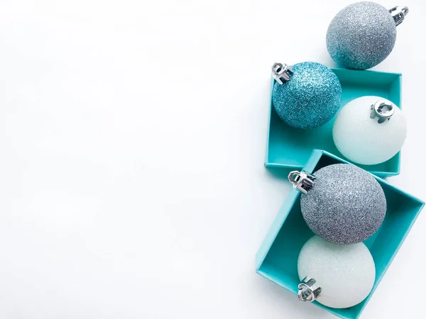 Turquoise jewel boxes inside of which is a shiny Christmas balls white, blue and silver color on the right. White background. Copy space.