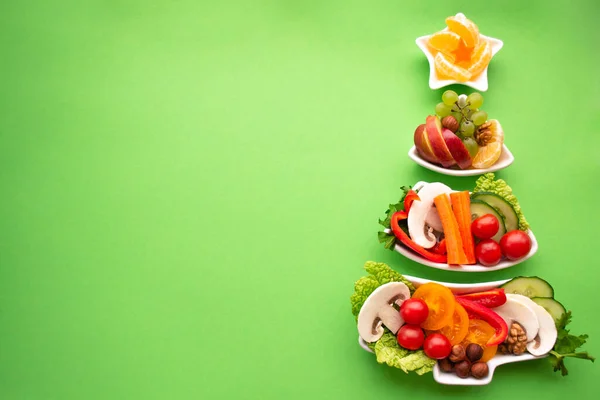 Sebze, meyve, mantar ve böğürtlenli bir Noel ağacı şeklinde tabak. Yeşil arka plan. Tatil için vejetaryen ziyafeti konsepti. Boşluğu kopyala.
