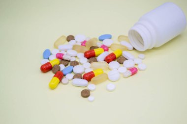 Sarı arka planda beyaz bir şişeden çok renkli haplar düşüyor..