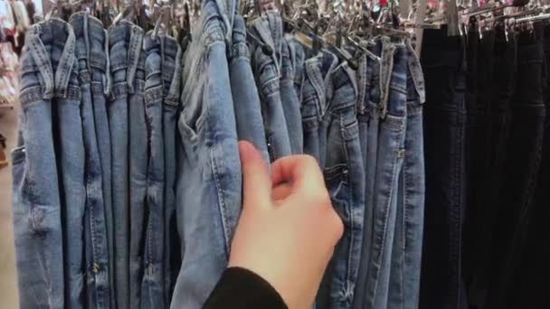 一个年轻女人或青少年的手正在从挂在服装店里的牛仔裤中挑选合适的牛仔裤 — 图库视频影像
