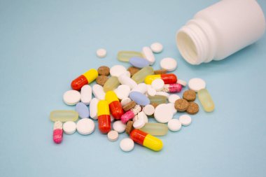 Mavi arka planda beyaz bir şişeden çok renkli haplar düşüyor..