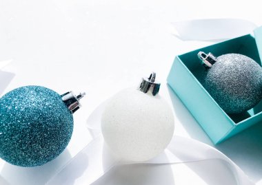 Parlak Noel toplarının yakın çekimi mavi turkuaz, beyaz ve gümüş renkli, kurdeleli ve beyaz arka planda mavi hediye kutusu. Noel ve tatil arifesi kavramı.