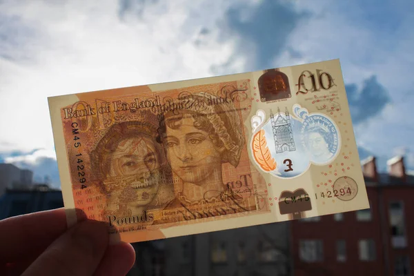 Moskova, Rusya, Şubat 2020: El, Kraliçe ve Jane Austen 'in portresi ile polimer plastikten yapılmış yepyeni bir 10 sterlin ve banknotun içinden geçen şeffaf bir pencereden yansıyan güneş ışığını elinde tutuyor..