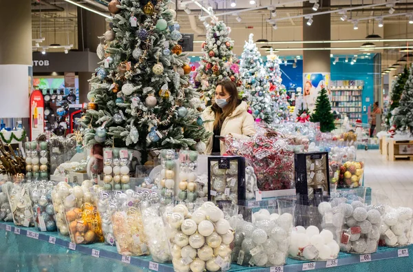 Moskova, Rusya, Kasım 2020: Genç maskeli bir kadın bir alışveriş merkezinde Noel oyuncaklarına bakıyor ve onları seçiyor.