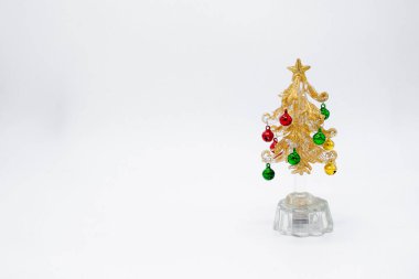 Taşak şeklinde yeşil ve kırmızı çanları olan, altın tozlu bir Noel ağacının cam saydam figürü. Beyaz arka plan. Boşluğu kopyala.