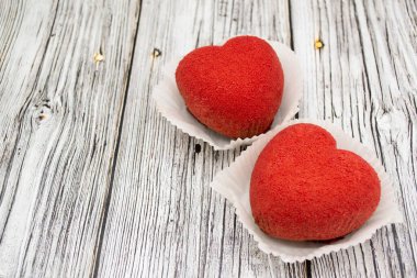 Ahşap arka planda parlak kırmızı kalp şeklinde kekler. Boşluğu kopyala.