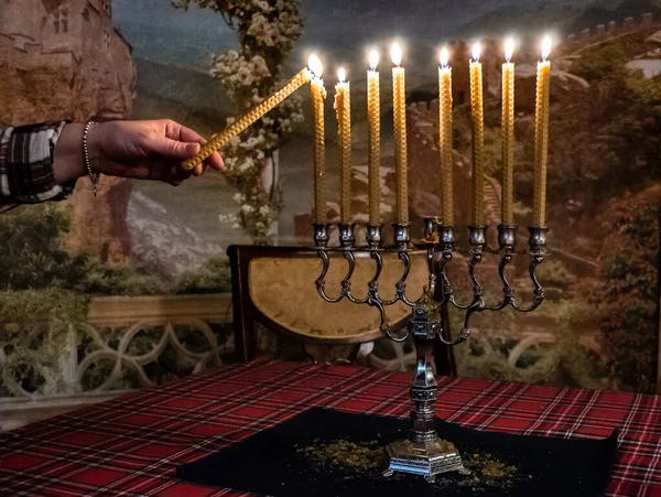 Hand holding a lit candle, lights eight candles on Hanukkah holiday.