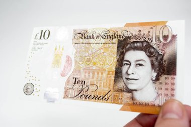 El, üzerinde Kraliçe 'nin portresi olan polimer plastikten yapılmış yepyeni bir 10 pound tutuyor. Beyaz arkaplan.