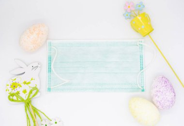 Tıbbi yüz maskesi, renkli yumurtalar, çiçekli bir kova ve Paskalya Tavşanı şeklinde süslemeler. Covid-19 salgını ve karantinası sırasında tatil kavramı.