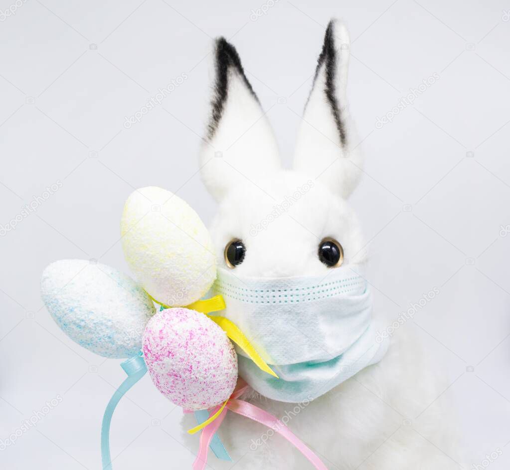 Close up Easter Bunny face in a medical mask with a bouquet of colorful eggs. The concept of Easter and quarantine during coronavirus. Like a postcard wishing you well.