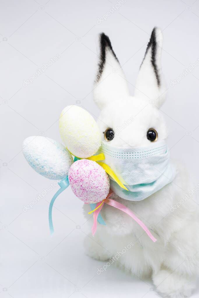 Easter Bunny in a facial medical mask with a bouquet of colorful eggs. The concept of Easter and quarantine during coronavirus. Like a postcard wishing you well.