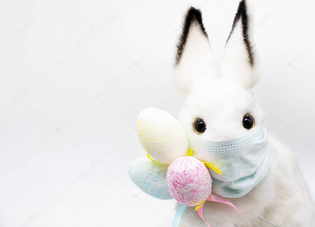 Close up Easter Bunny face in a medical mask with a bouquet of colorful eggs. The concept of Easter and quarantine during coronavirus. Like a postcard wishing you well.