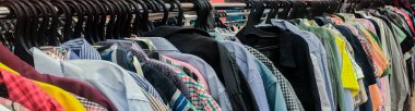 İkinci el mağazasındaki askılarda bir sürü renkli tişörtle afiş. Ucuz alışveriş konsepti, Kara Cuma.