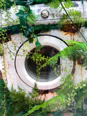 MOSCOW, Rusya, Şubat 2021: Çim ve bitkilerle kaplanmış eski paslı bir çamaşır makinesi. Ev aletlerine karşı ekolojik tutum ve doğanın medeniyete karşı zaferi..