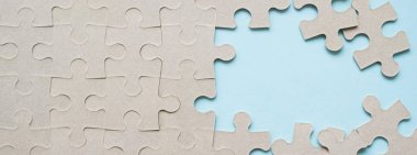 Tamamlanmamış mukavva yapbozlu afiş. Sağda mavi bir arkaplan ve bulmacanın birkaç dağınık parçası. Boşluğu kopyala.