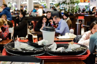 Moskova, Rusya, Kasım 2019: Arta kalan yemekler, plastik kaplar ve bir alışveriş merkezinde yemek yiyen insanların bulanık arka planında bir fincan kahvenin olduğu tepsilerin yakın çekimi.
