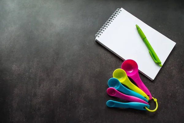 Multi Colored Measuring Spoons Notebook White Pages Green Pen Writing — Stock Photo, Image