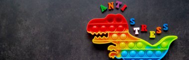 Oyuncak pankartı siyah arkaplanda dinozor gökkuşağı renginde ve arkasında çok renkli harfler ve gerilim önleyici yazılar var. Boşluğu kopyala.