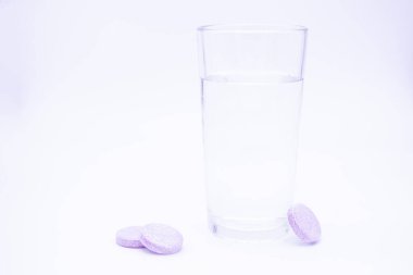 Yanında temiz su bulunan şeffaf cam bardaklar. Pembe tabletler, C vitamini, diyet takviyeleri, ağrı kesiciler..