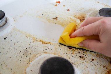 Sarı bir süngeri olan bir el gaz sobasının çok kirli yüzeyini yıkar. Süngerden sonra, temiz bir iz kalır..