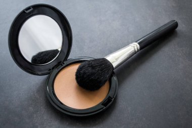 Siyah makyaj fırçası ve aynalı açık pembe toz kutusu. Siyah arka plan. Boşluğu kopyala.