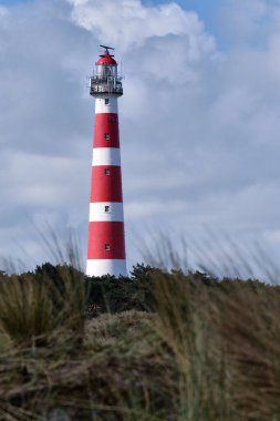 Klasik, tarihi kırmızı ve beyaz deniz feneri, kumullar ve çimenler, güneşli bir gün ve Hollanda 'nın Ameland adasında çalkantılı bulutlar, Hollum, Nisan 2021