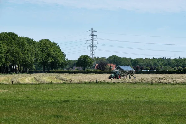 Dronten, 1 juni 2021: Grasland met tractormaaier en -hark, gras klaar voor teelt.Nederlandse boeren racen tegen de regen om hooi, maaien, harken en kuil.Alle boeren werken op het land — Stockfoto