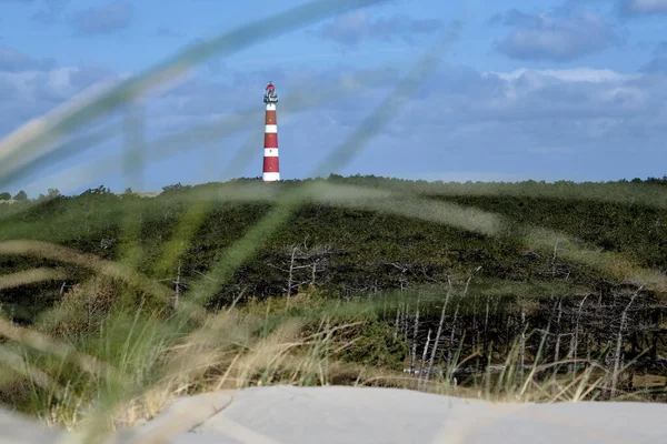 Klasik, tarihi kırmızı ve beyaz deniz feneri, kumullar ve çimenler, güneşli bir gün ve Hollanda 'nın Ameland adasında çalkantılı bulutlar, Hollum, Nisan 2021