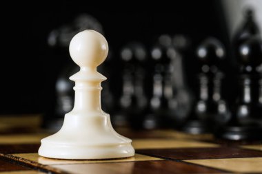 Siyah satranç taşlarına karşı yakın plan beyaz piyon. Yüzleşme konsepti, yalnızlık..