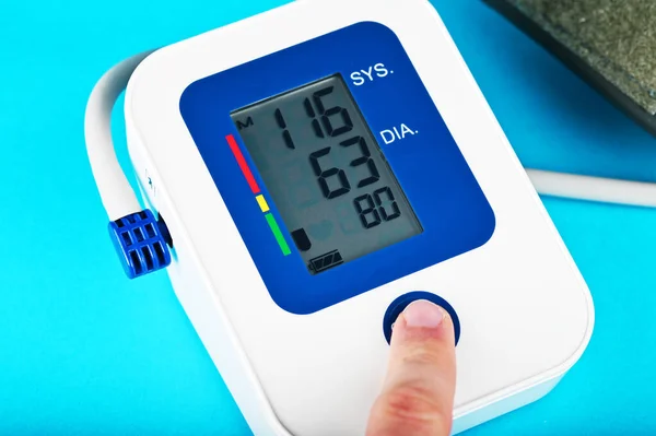 Mężczyzna palec wskazujący naciska przycisk cyfrowy ciśnieniomierz na niebieskim tle zbliżenie pokazuje normalne ciśnienie krwi Zdjęcie Stockowe