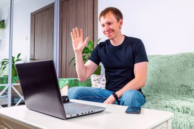 Genç bir adam evde günlük kıyafetleriyle bilgisayar üzerinden iletişim kuruyor.