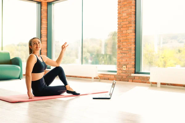 Uma mulher atlética esbelta é treinadora. Ela treina em vídeo na internet, um treinamento on-line em laptop moderno sendo instrutor de ioga. Meditação, conceito de estilo de vida saudável. — Fotografia de Stock