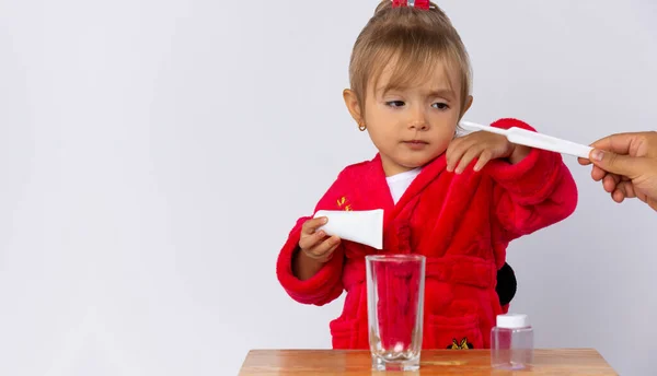 Linda niña con una pasta de dientes y un cepillo en la mano, soñolienta se prepara para cepillarse los dientes. La higiene dental debe ser observada desde la infancia. Concepto sobre fondo gris claro con espacio en blanco — Foto de Stock