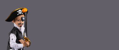 Banner, uzun format. Korsan kostümü giymiş, elinde kılıç olan küçük bir çocuk balkabağı yakalar. Gri arka planda Cadılar Bayramı konsepti. Yüksek kalite fotoğraf