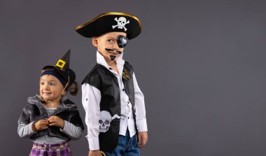 Mutlu çocuklar, korsan çocuk ve Cadılar Bayramı için küçük cadı. Karnaval kostümlü çocuklar arka planda gri bir arka planda ve boş bir yan alanı var. Yüksek kalite fotoğraf