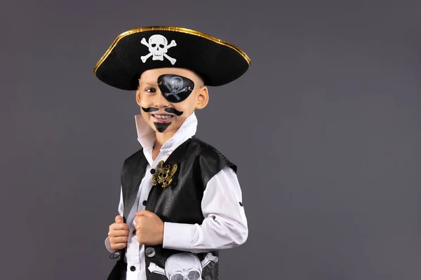 Yüzü makyajlı bir korsan gibi giyinmiş küçük çocuk Cadılar Bayramı partisinde eğleniyor. Çocuklar için yüz boyama. Boş alan ile izole edilmiş gri arkaplan. Yüksek kalite fotoğraf