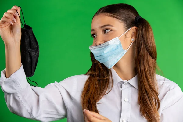 一个戴着医疗面罩 手里拿着另一个备用物品的可爱女生 在绿色的背景上被隔离 病毒和流行病的概念 高质量的照片 — 图库照片