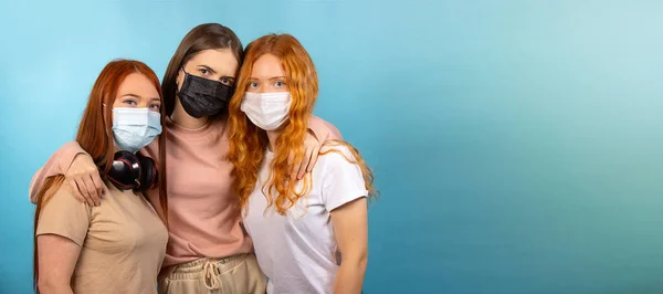 长格式 社会距离 三个女朋友互相拥抱着 还戴着口罩 以防止这种流行病的蔓延 蓝色背景上的照片 侧面有很大的空间 高质量的照片 — 图库照片