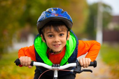 Kaskla poz veren ve gülümseyen bir çocuğun portresi ve sonbahar parkında bisiklet pedalı. Aktif, sağlıklı açık hava sporları. Yüksek kalite fotoğraf