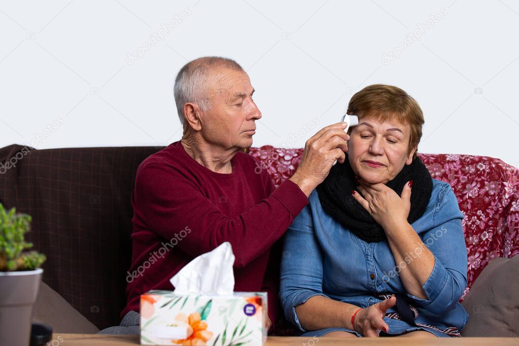 The husband takes care of his sick wife, measures the temperature with a non-contact thermometer. An elderly couple is fighting a viral infection and sore throat at home. Covid 19 concept