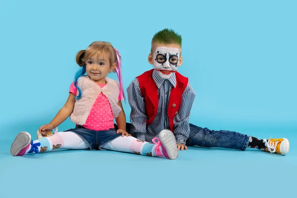 Söt pojke och flicka på Halloween. Barn sitter på tvinnat garn och ler glatt. Halloween foto på blå bakgrund — Stockfoto