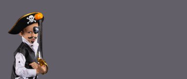  Korsan kostümü giymiş, elinde kılıç olan küçük bir çocuk balkabağı yakalar. Cadılar Bayramı konsepti.