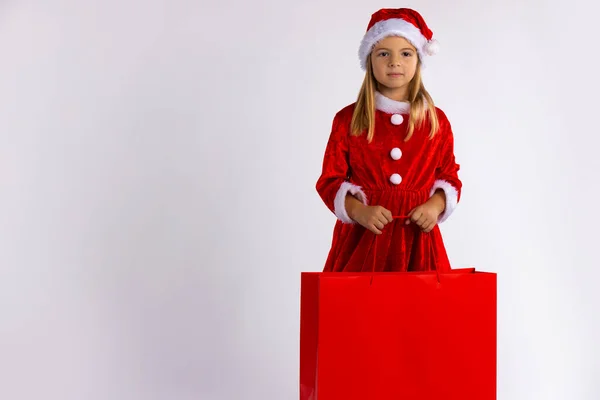 Маленькая девочка в красном платье и в красной шляпе Санта-Клауса, с подарочной сумкой в руках. — стоковое фото
