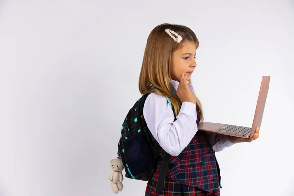 Jolie petite fille en uniforme scolaire tenant un ordinateur portable montrant bonjour isolé sur fond gris. Concept d'apprentissage en ligne. — Photo