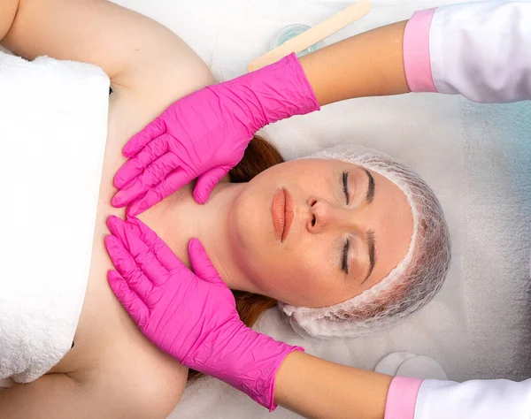 Close-up de uma jovem mulher recebendo uma massagem facial cosmética em um salão de beleza e as mãos do mestre em luvas são visíveis. Cuidados faciais. Spa. — Fotografia de Stock