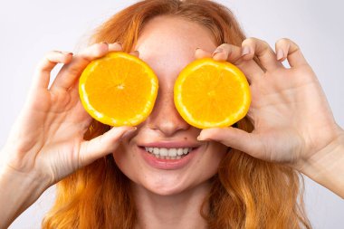 Güzel kızıl saçlı, neşeli, çilli, kırmızı bukleli ve sarı makyajlı kız. Portakal dilimleri, kahkahalar, duygular. Güzellik ve güzellik konsepti.